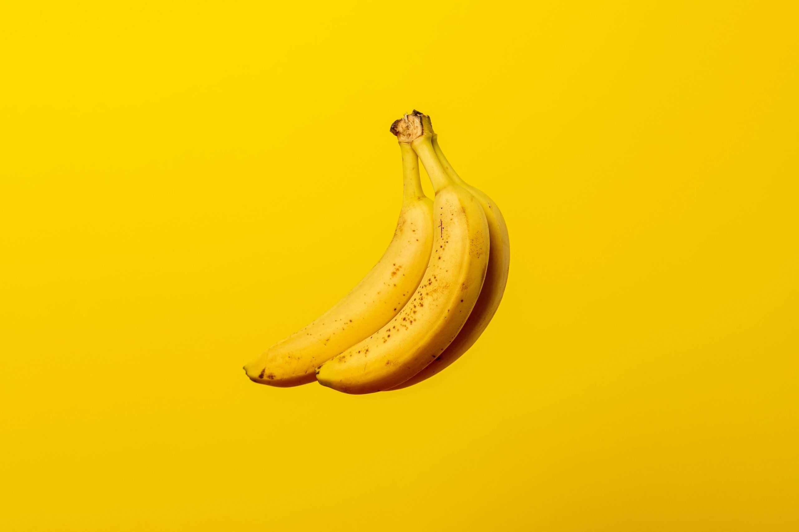 A bunch of ripe yellow bananas against a vivid yellow backdrop, offering tropical freshness.