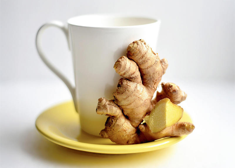 Taza blanca sobre plato amarillo con raíz de jengibre fresco